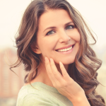Smiling woman tilts head and gently touches face with hand