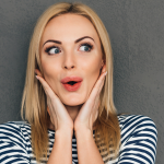 Woman with smooth skin and full, red lips looks surprised with hands on either side of face