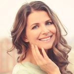 Woman smiling lightly touching her smooth cheek with her hand