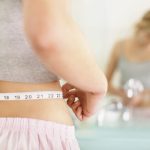 Woman measuring her waist reflected in mirror