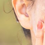 woman with red nails touching the brown spots on her cheek (model)