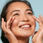 Woman with beautiful skin smiling and lightly touching under her eyes (model)