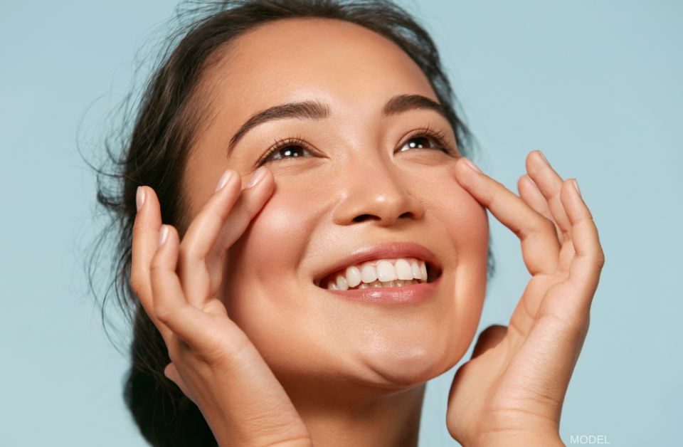 Woman with beautiful skin smiling and lightly touching under her eyes (model)